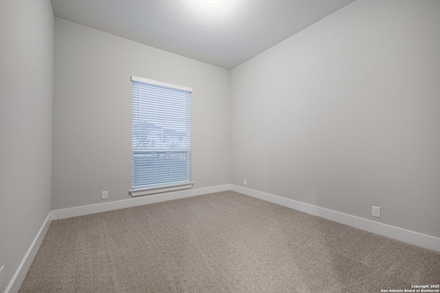 spare room featuring light carpet, baseboards, and a textured ceiling