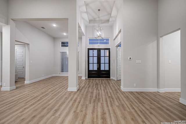 entrance foyer with a towering ceiling, light wood-style flooring, baseboards, and french doors