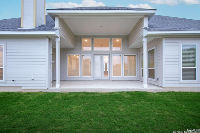 back of house with a patio, a shingled roof, and a lawn