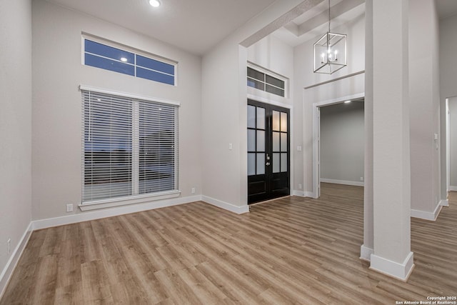 entryway with a towering ceiling, a notable chandelier, baseboards, and wood finished floors