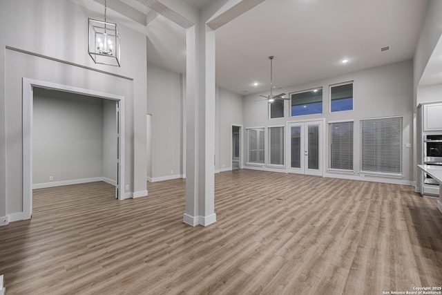 unfurnished living room with light wood-style floors, baseboards, a high ceiling, and ceiling fan with notable chandelier