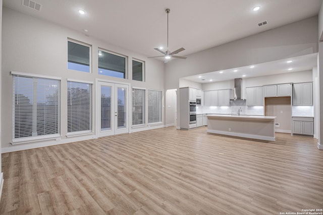 unfurnished living room featuring visible vents, light wood-style flooring, a high ceiling, a sink, and ceiling fan