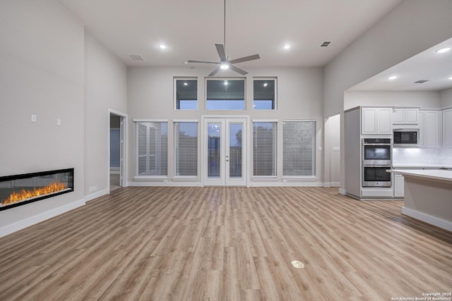 unfurnished living room featuring light wood-style flooring, visible vents, and a glass covered fireplace