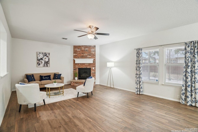 living room with ceiling fan, wood finished floors, visible vents, baseboards, and a brick fireplace