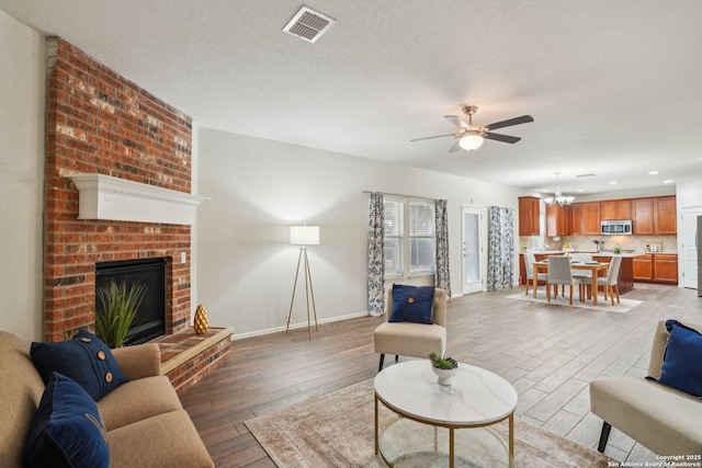 living room featuring a fireplace, visible vents, light wood-style flooring, a textured ceiling, and baseboards