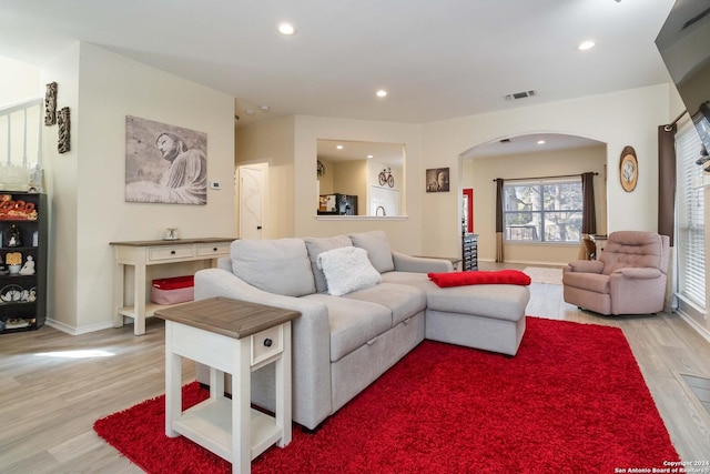 living area featuring arched walkways, visible vents, light wood finished floors, and recessed lighting