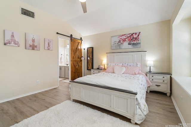 bedroom with light wood-style floors, visible vents, vaulted ceiling, and a barn door