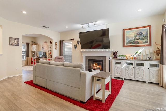 living room with arched walkways, light wood finished floors, a fireplace, and visible vents