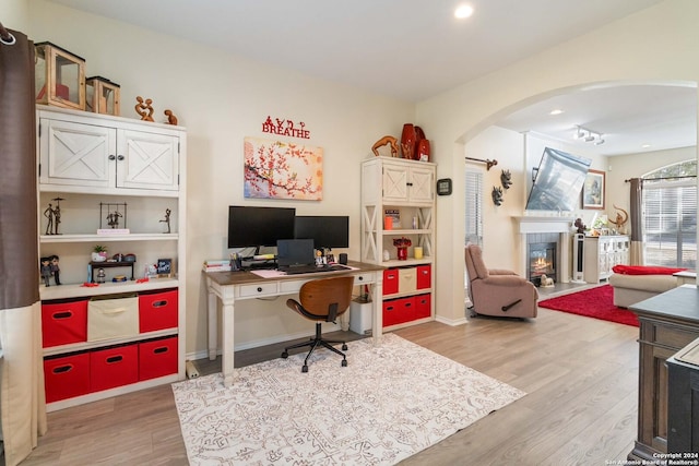 office space featuring light wood-style floors, arched walkways, a glass covered fireplace, and baseboards