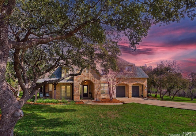 view of front facade featuring a garage, concrete driveway, french doors, stone siding, and a front yard