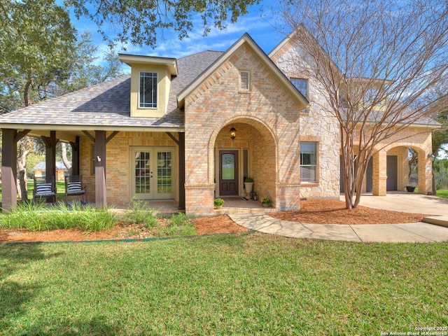 view of front of house with brick siding, concrete driveway, french doors, roof with shingles, and a front yard