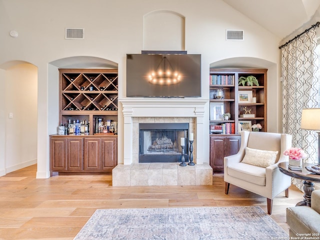 living room featuring built in features, a tile fireplace, visible vents, and wood finished floors