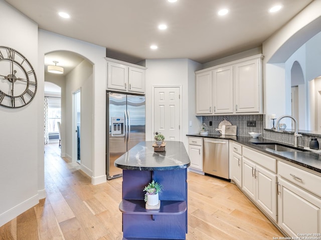 kitchen with light wood finished floors, arched walkways, decorative backsplash, appliances with stainless steel finishes, and a sink