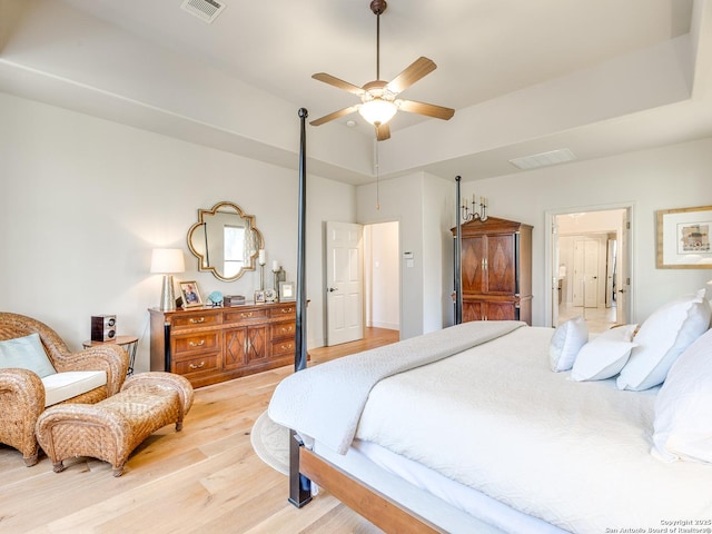 bedroom featuring light wood finished floors, visible vents, and a raised ceiling