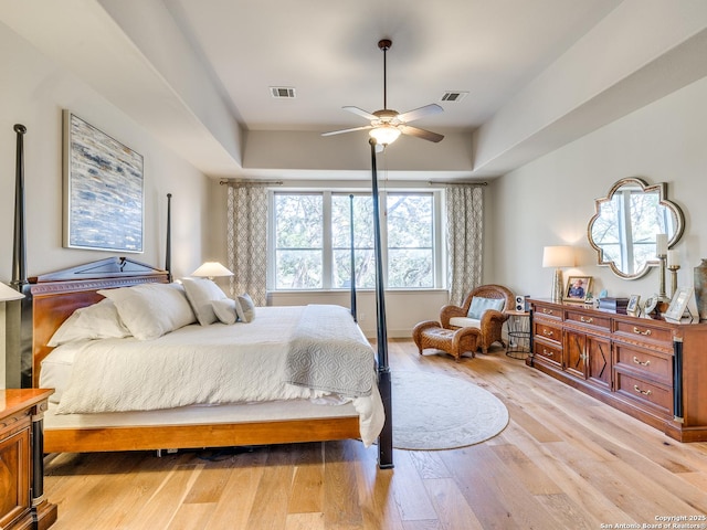 bedroom with light wood-type flooring, visible vents, a tray ceiling, and ceiling fan