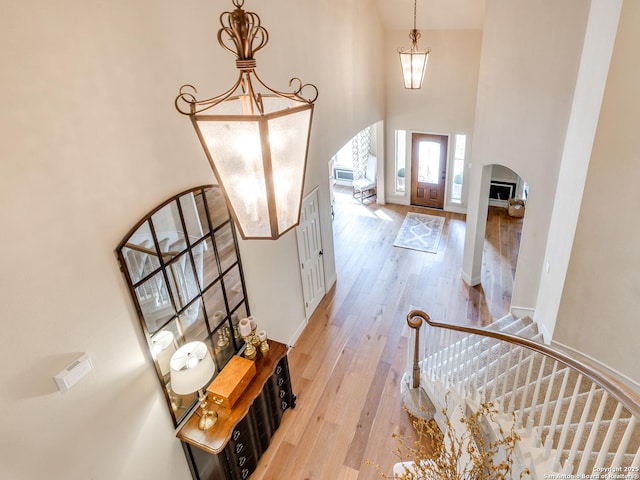 foyer with arched walkways, a high ceiling, light wood-type flooring, and stairs