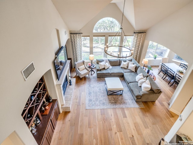 living area featuring a notable chandelier, a wealth of natural light, visible vents, light wood-style flooring, and high vaulted ceiling