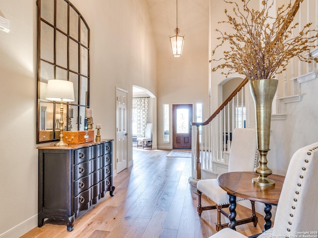 entrance foyer featuring light wood finished floors, baseboards, arched walkways, a towering ceiling, and stairway