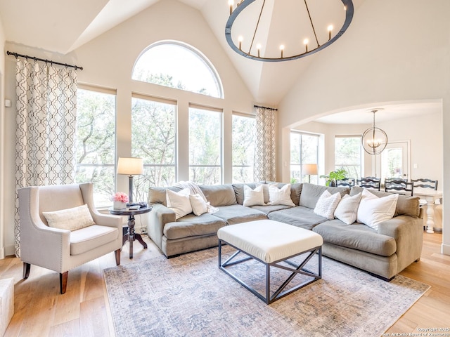 living area featuring high vaulted ceiling, arched walkways, wood finished floors, and an inviting chandelier