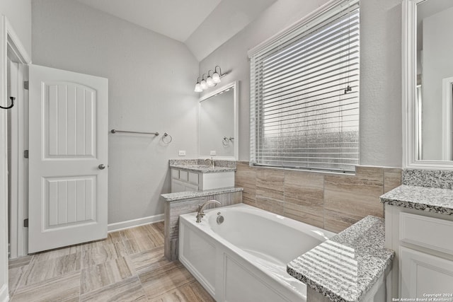 full bathroom featuring lofted ceiling, a garden tub, and vanity