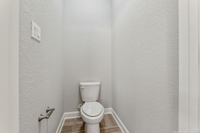 bathroom featuring a textured wall, wood finished floors, toilet, and baseboards