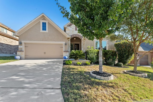 traditional-style house with driveway, a garage, stone siding, stucco siding, and a front yard