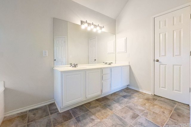 full bath with lofted ceiling, double vanity, a sink, and baseboards