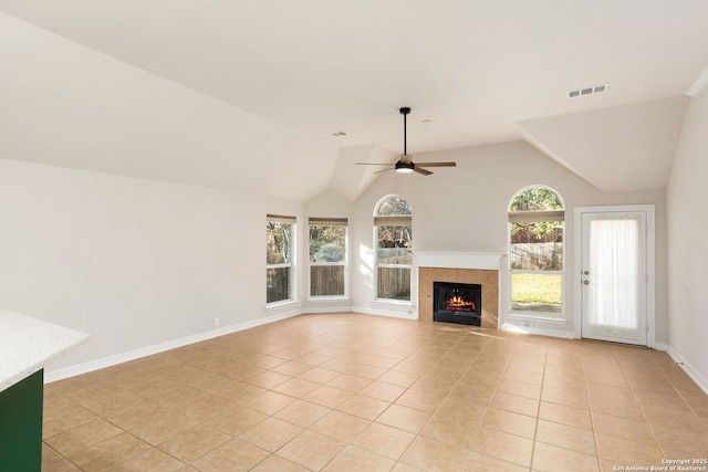 unfurnished living room featuring a ceiling fan, a wealth of natural light, a warm lit fireplace, and visible vents