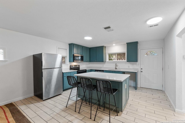 kitchen with stainless steel appliances, light countertops, blue cabinetry, a kitchen bar, and a sink