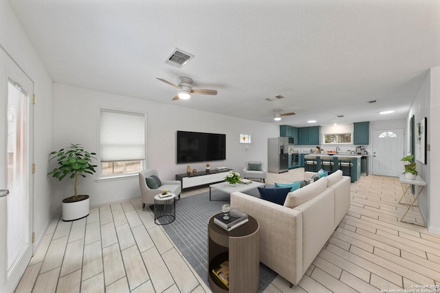 living area with visible vents, a ceiling fan, and wood finish floors