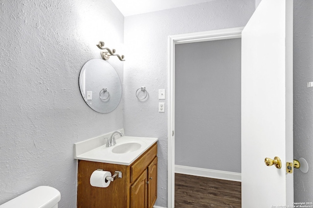 bathroom featuring a textured wall, toilet, vanity, wood finished floors, and baseboards