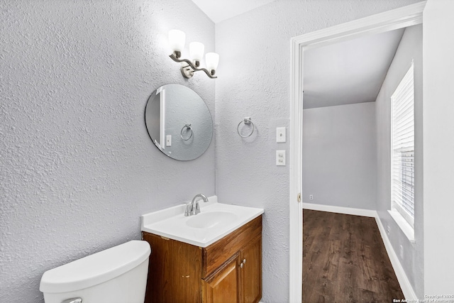 bathroom with toilet, a textured wall, vanity, and baseboards