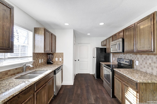 kitchen featuring light stone counters, stainless steel appliances, a sink, baseboards, and dark wood finished floors