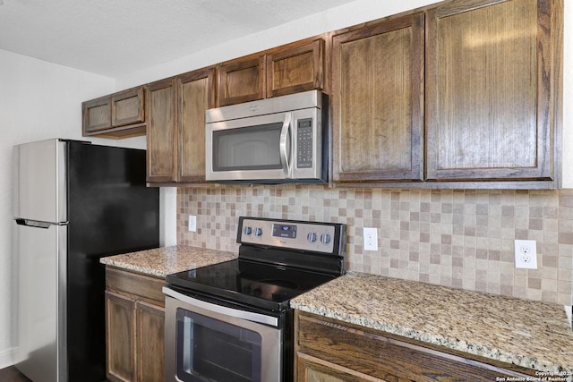 kitchen featuring appliances with stainless steel finishes, light stone counters, decorative backsplash, and a textured ceiling