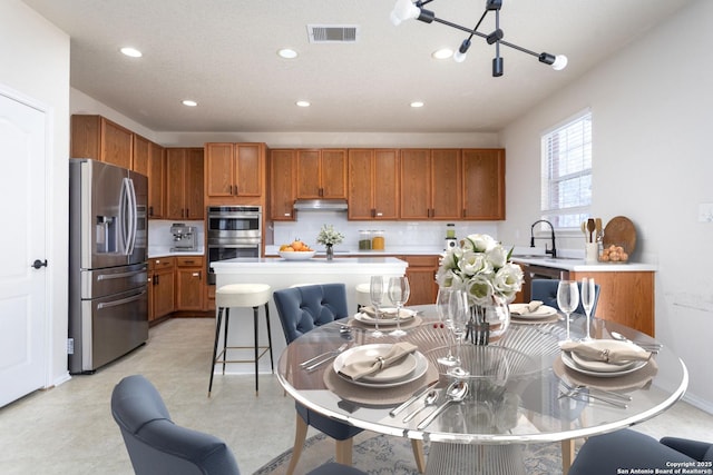 kitchen with visible vents, brown cabinetry, appliances with stainless steel finishes, light countertops, and under cabinet range hood