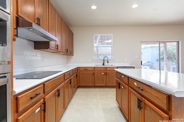 kitchen featuring light countertops, a healthy amount of sunlight, a sink, and under cabinet range hood