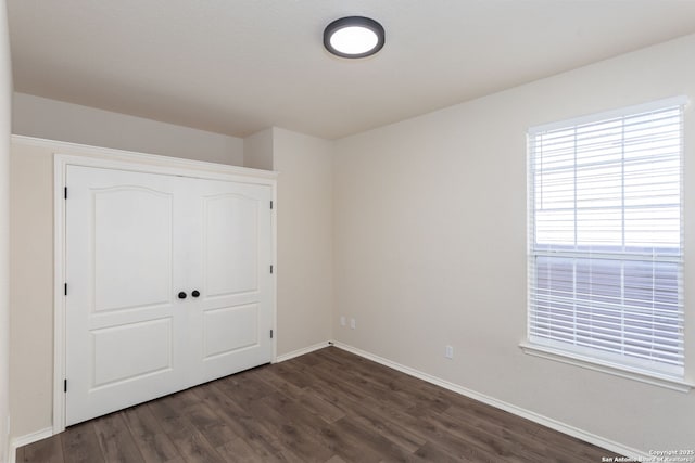 unfurnished bedroom with dark wood-style floors, baseboards, and a closet