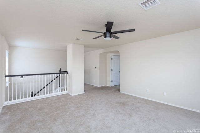 carpeted empty room with arched walkways, ceiling fan, a textured ceiling, visible vents, and baseboards