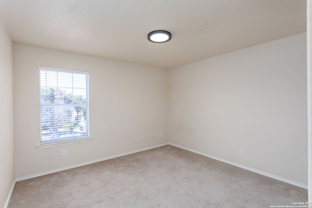 spare room with light carpet, baseboards, and a textured ceiling