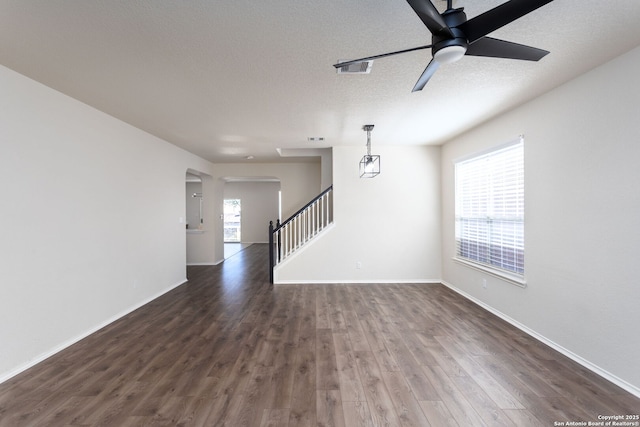 unfurnished living room featuring dark wood-style flooring, plenty of natural light, stairway, and a textured ceiling