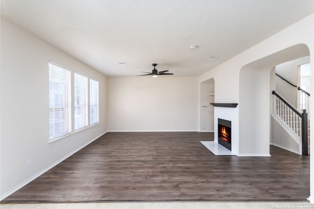 unfurnished living room featuring a fireplace with flush hearth, a ceiling fan, baseboards, stairs, and dark wood-style floors