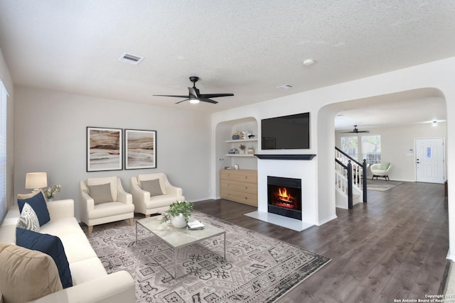 living area featuring a textured ceiling, a fireplace with flush hearth, wood finished floors, and a ceiling fan