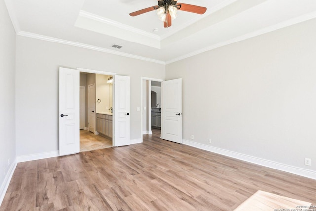 unfurnished bedroom featuring visible vents, a tray ceiling, light wood-style flooring, and baseboards