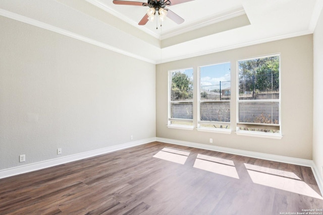 unfurnished room with baseboards, a tray ceiling, wood finished floors, and crown molding