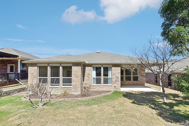 back of property featuring brick siding, a shingled roof, a sunroom, a yard, and a patio area