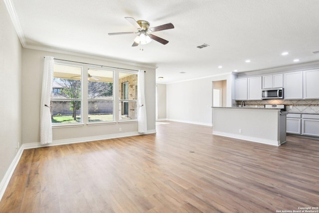 unfurnished living room with ornamental molding, light wood-type flooring, visible vents, and baseboards