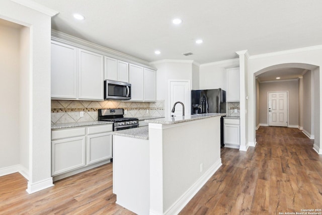 kitchen featuring arched walkways, light wood-style flooring, a kitchen island with sink, visible vents, and appliances with stainless steel finishes