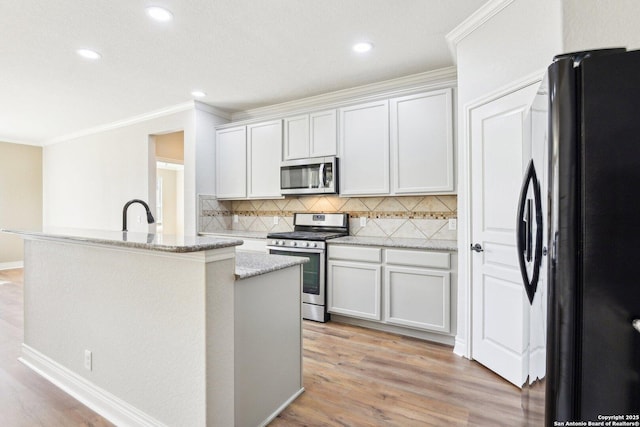 kitchen featuring a center island with sink, ornamental molding, stainless steel appliances, light wood-type flooring, and backsplash