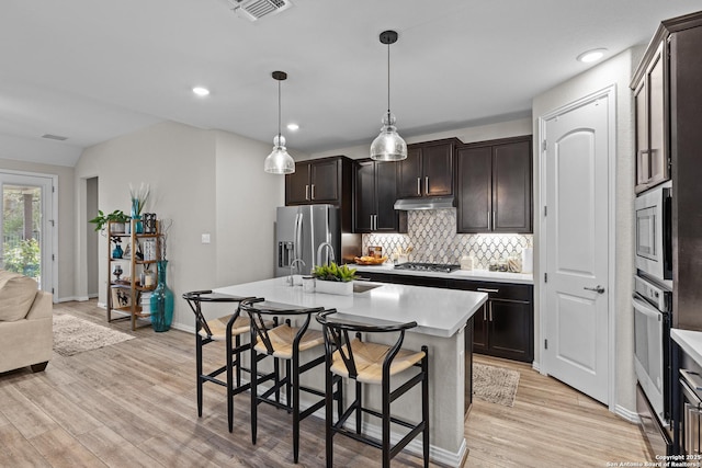 kitchen featuring a breakfast bar, stainless steel appliances, light countertops, decorative backsplash, and a sink