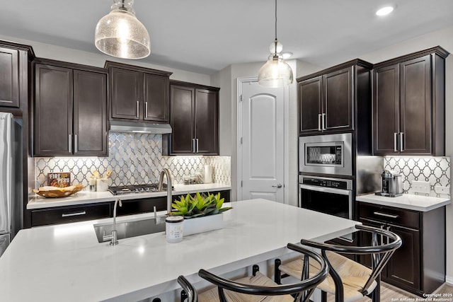 kitchen featuring appliances with stainless steel finishes, hanging light fixtures, light countertops, dark brown cabinets, and a kitchen bar